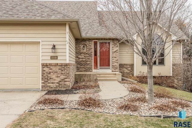 doorway to property with brick siding, driveway, a shingled roof, and a garage