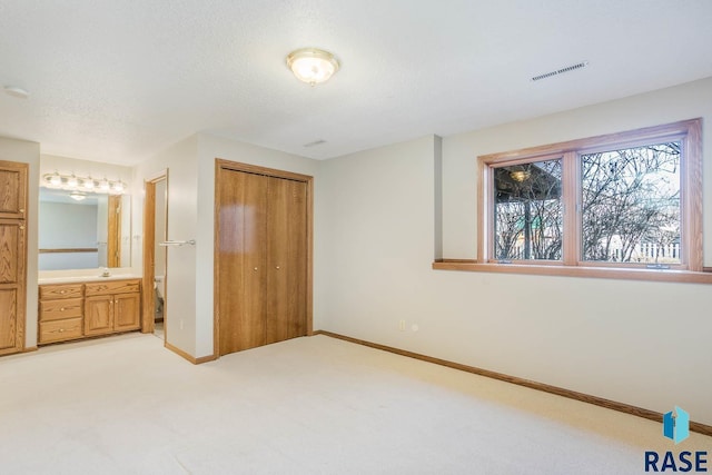 unfurnished bedroom with a textured ceiling, a closet, visible vents, light carpet, and baseboards