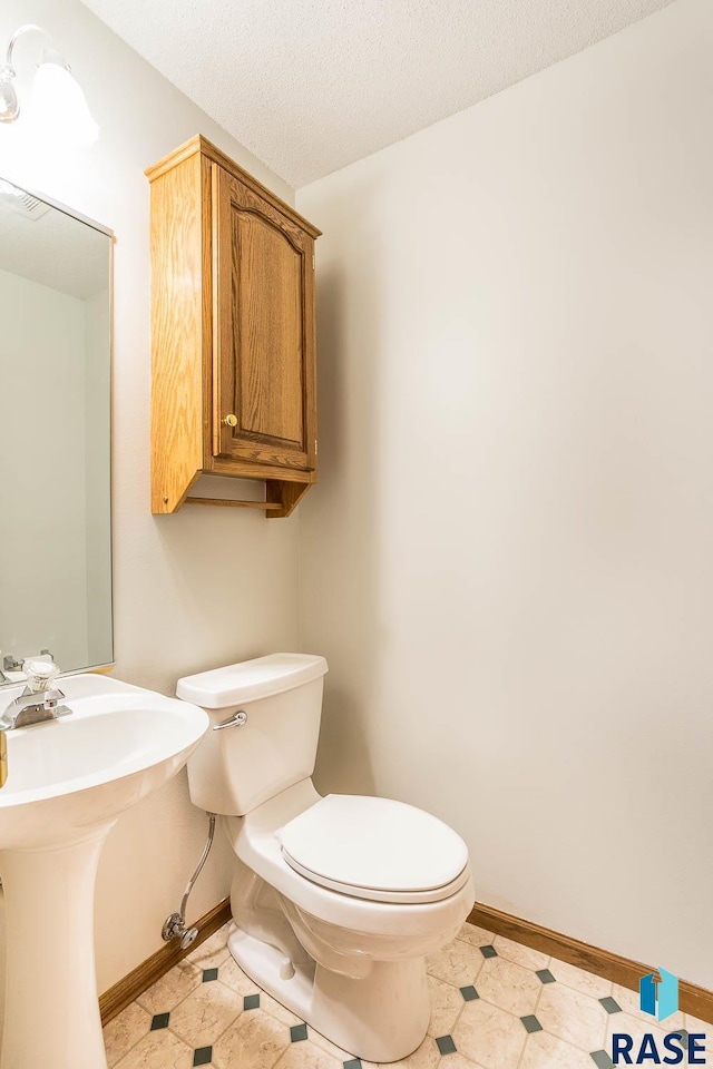 half bath featuring tile patterned floors, toilet, baseboards, and a textured ceiling