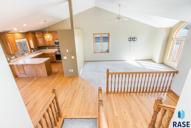 kitchen featuring open floor plan, appliances with stainless steel finishes, a ceiling fan, light wood finished floors, and vaulted ceiling