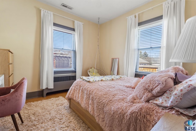 bedroom featuring radiator, baseboards, wood finished floors, and visible vents