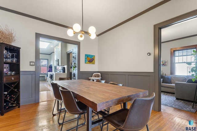 dining room featuring light wood finished floors, wainscoting, an inviting chandelier, a decorative wall, and ornamental molding
