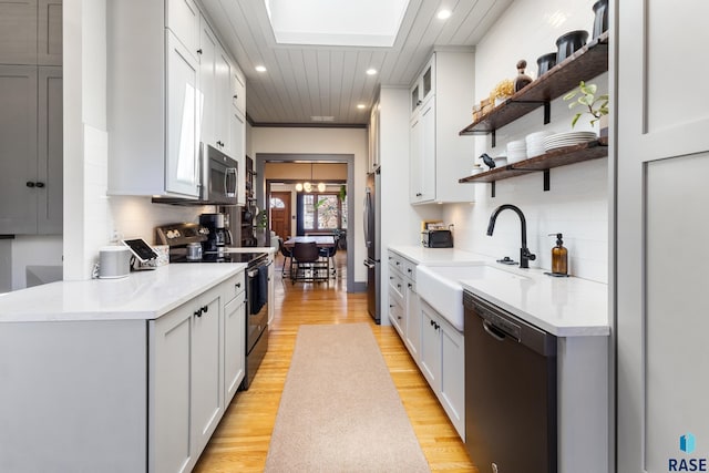kitchen with open shelves, light wood-style floors, stainless steel appliances, light countertops, and backsplash