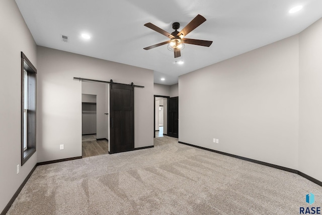 unfurnished bedroom with light colored carpet, visible vents, recessed lighting, a barn door, and baseboards