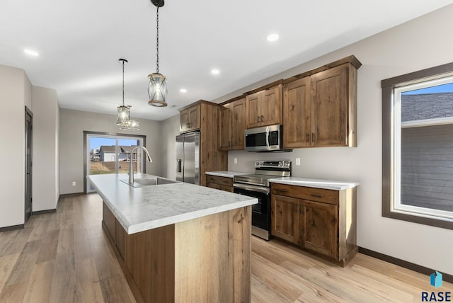 kitchen featuring stainless steel appliances, light wood finished floors, a sink, and an island with sink