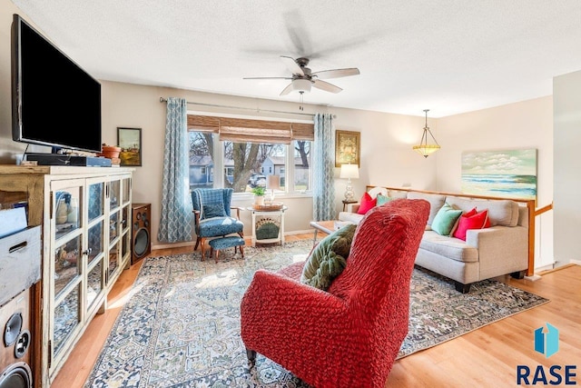 living area with a textured ceiling, wood finished floors, ceiling fan, and baseboards