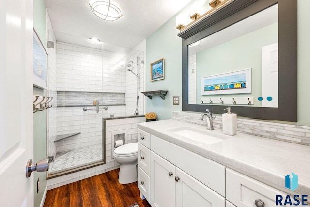 full bathroom with toilet, a textured ceiling, vanity, wood finished floors, and a stall shower