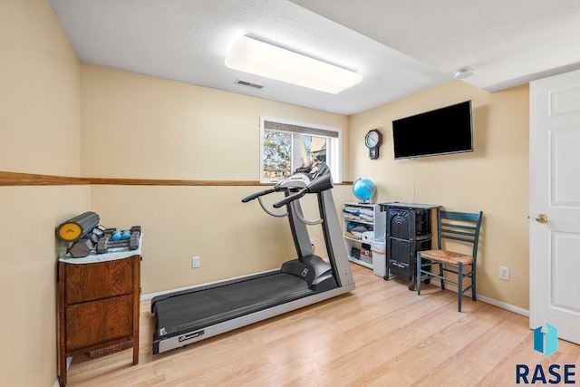 workout room featuring visible vents, a textured ceiling, baseboards, and wood finished floors
