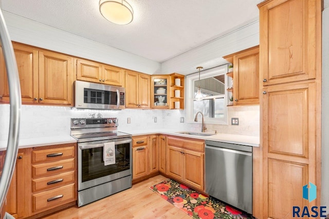 kitchen with open shelves, appliances with stainless steel finishes, light countertops, a sink, and light wood finished floors