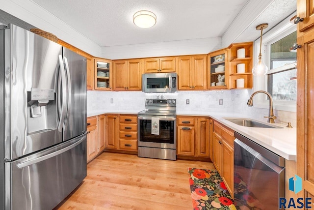 kitchen featuring a sink, light countertops, pendant lighting, stainless steel appliances, and light wood-style flooring