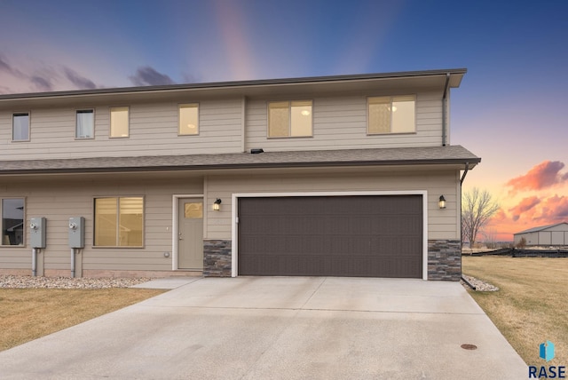 view of property with stone siding, a lawn, a garage, and concrete driveway