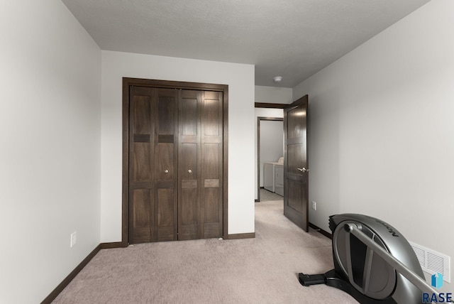 exercise room featuring washing machine and clothes dryer, light carpet, and baseboards