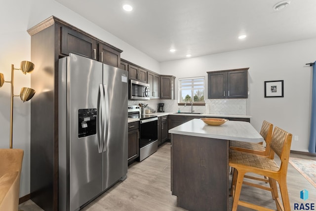 kitchen featuring a kitchen breakfast bar, tasteful backsplash, appliances with stainless steel finishes, light countertops, and a sink
