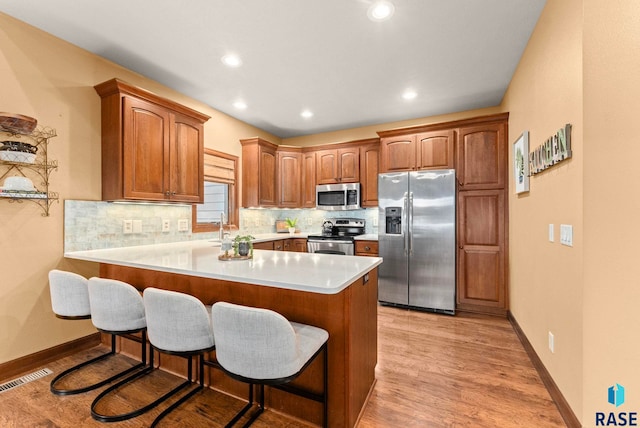 kitchen with tasteful backsplash, a peninsula, visible vents, appliances with stainless steel finishes, and a breakfast bar area