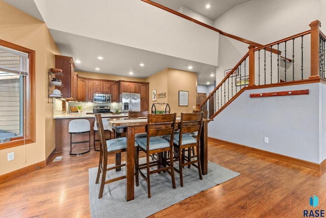 dining space with light wood-type flooring, a towering ceiling, recessed lighting, stairway, and baseboards