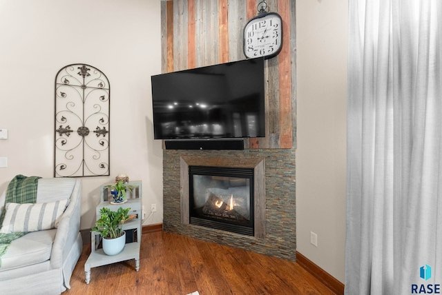 living area with a glass covered fireplace, baseboards, and wood finished floors