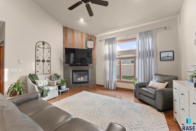 living room featuring baseboards, ceiling fan, vaulted ceiling, wood finished floors, and a large fireplace