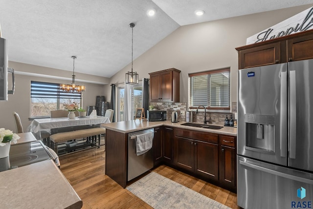 kitchen with vaulted ceiling, light countertops, a sink, stainless steel appliances, and a notable chandelier