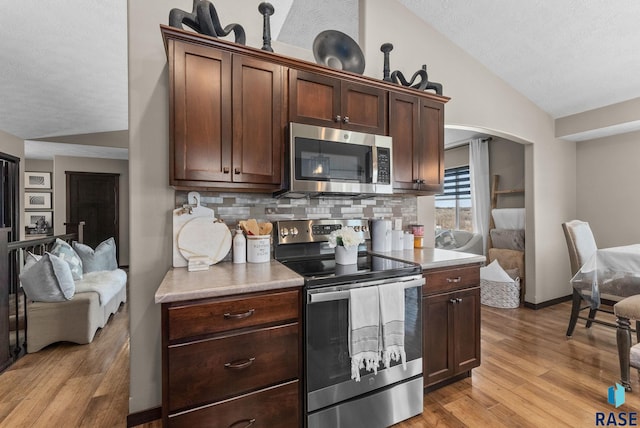 kitchen with arched walkways, vaulted ceiling, appliances with stainless steel finishes, light countertops, and light wood finished floors