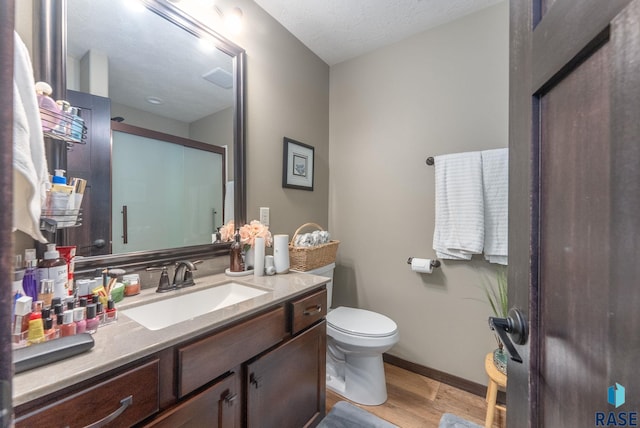bathroom featuring vanity, baseboards, toilet, a shower with shower door, and wood finished floors