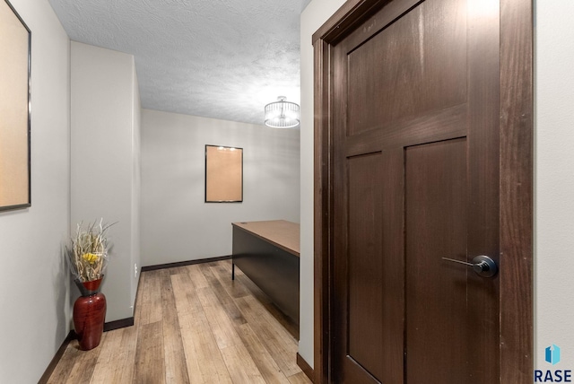 corridor featuring baseboards, light wood-style floors, and a textured ceiling
