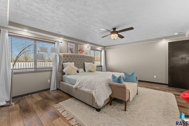 bedroom with hardwood / wood-style floors, baseboards, visible vents, and a textured ceiling