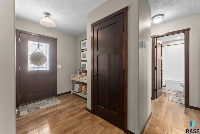 foyer with baseboards, light wood-style floors, and a textured ceiling
