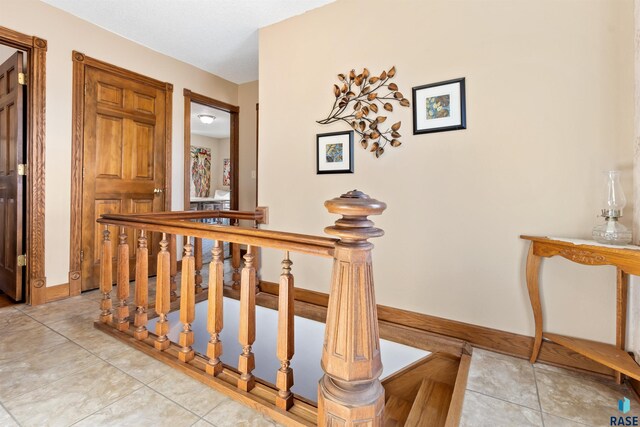 corridor with light tile patterned floors, baseboards, and an upstairs landing