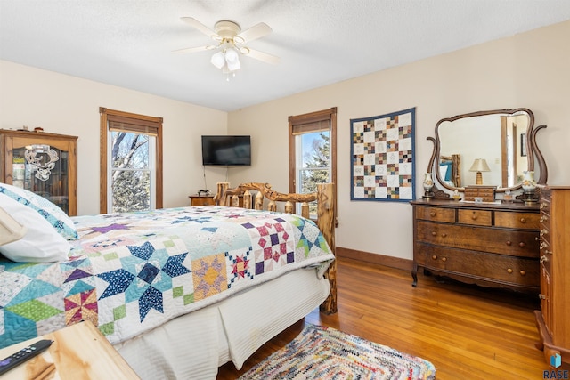 bedroom with a textured ceiling, wood finished floors, ceiling fan, and baseboards