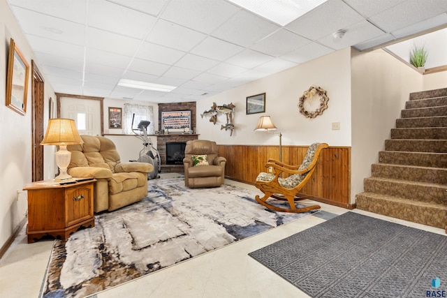living room with a paneled ceiling, a large fireplace, a wainscoted wall, wood walls, and stairs