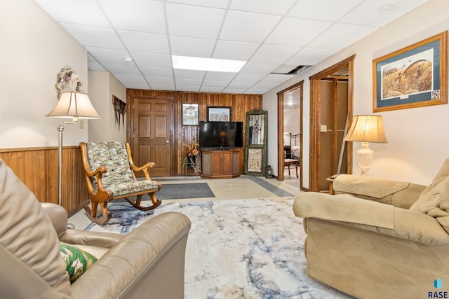 living area with wainscoting, wood walls, a drop ceiling, and visible vents