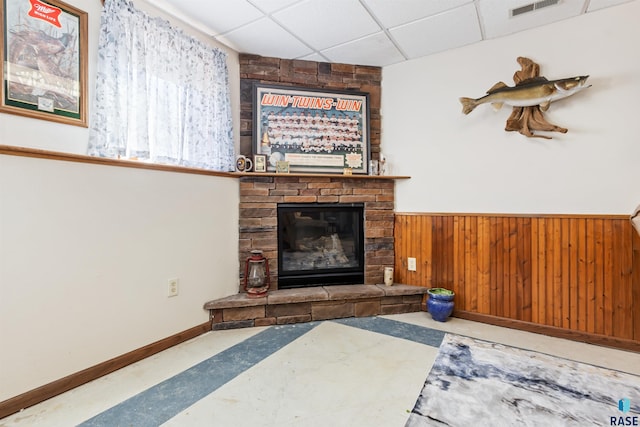 living area with a paneled ceiling, a fireplace, a wainscoted wall, wood walls, and visible vents