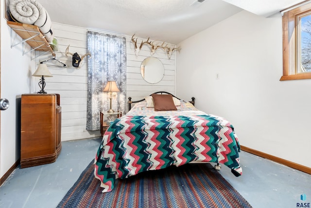 bedroom featuring concrete flooring, wood walls, and baseboards