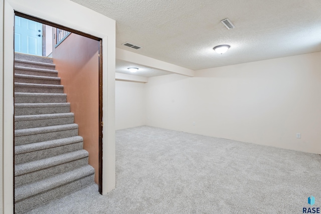 finished basement featuring visible vents, a textured ceiling, carpet, and stairs