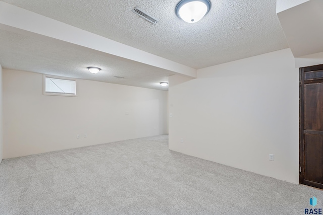 below grade area with carpet, visible vents, and a textured ceiling