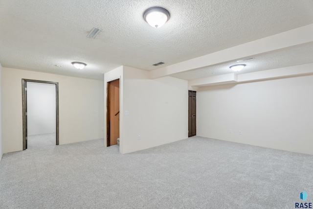 finished below grade area featuring visible vents, light carpet, and a textured ceiling