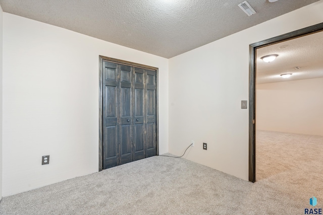 unfurnished bedroom featuring a textured ceiling, a closet, visible vents, and carpet