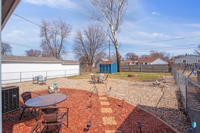 view of yard featuring central AC unit, a shed, a fenced backyard, outdoor dining space, and an outbuilding