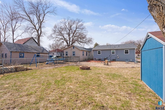 rear view of house featuring a lawn, a fire pit, fence, a playground, and a trampoline