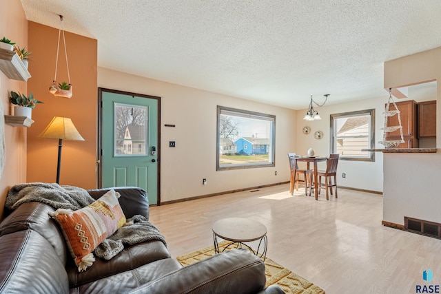 living area with visible vents, a textured ceiling, baseboards, and light wood-style flooring
