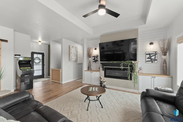 living room featuring a glass covered fireplace, a barn door, ceiling fan, a raised ceiling, and wood finished floors