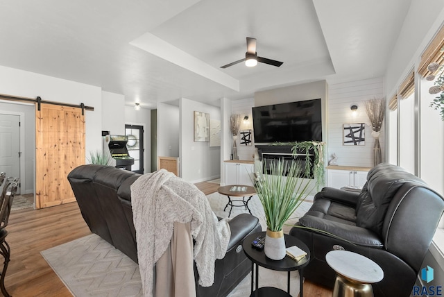 living room featuring baseboards, a raised ceiling, a barn door, ceiling fan, and wood finished floors
