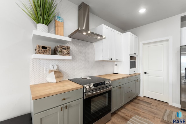 kitchen featuring wall chimney exhaust hood, light wood-style flooring, open shelves, stainless steel appliances, and wooden counters
