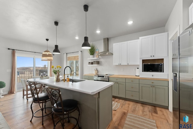 kitchen featuring light wood-type flooring, wall chimney range hood, appliances with stainless steel finishes, decorative backsplash, and a breakfast bar area