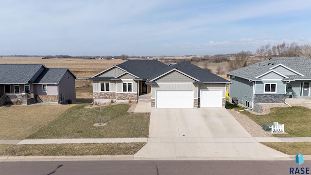 view of front facade featuring board and batten siding, a garage, stone siding, a front lawn, and concrete driveway