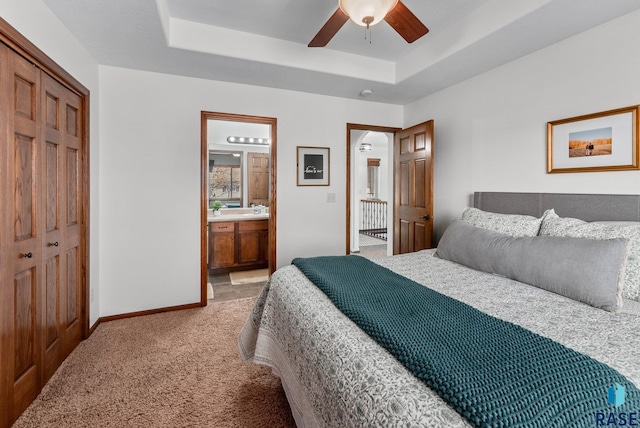 bedroom featuring ensuite bathroom, a closet, light colored carpet, a raised ceiling, and baseboards