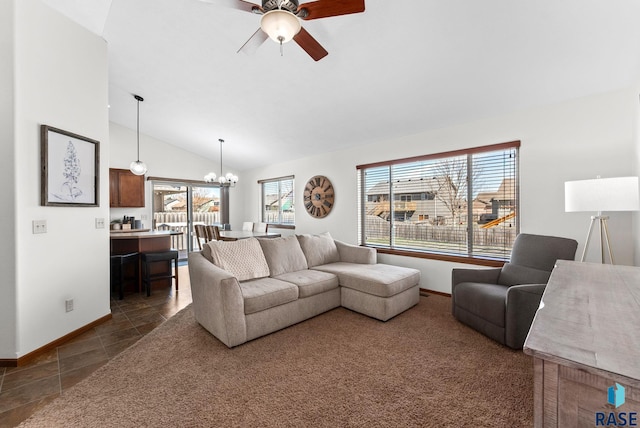 living area with baseboards, ceiling fan with notable chandelier, dark tile patterned floors, and vaulted ceiling