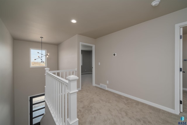 hallway with visible vents, baseboards, an inviting chandelier, an upstairs landing, and light colored carpet