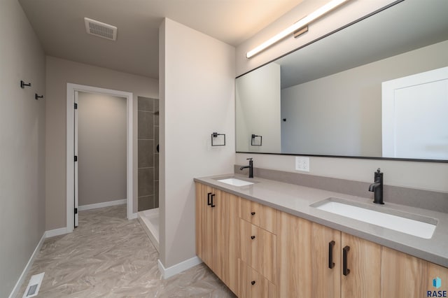bathroom with a sink, visible vents, a tile shower, and baseboards