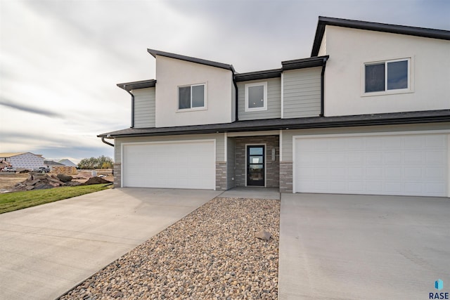view of front of house featuring an attached garage, stone siding, driveway, and stucco siding